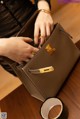 A woman holding a brown handbag on a wooden table.