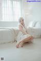 A woman sitting on a bed in a white room.