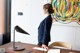 A woman standing at a desk in front of a painting.