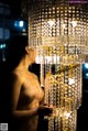 A naked woman standing in front of a chandelier.