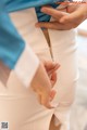 A woman in a blue shirt and white pants is putting on a zipper.