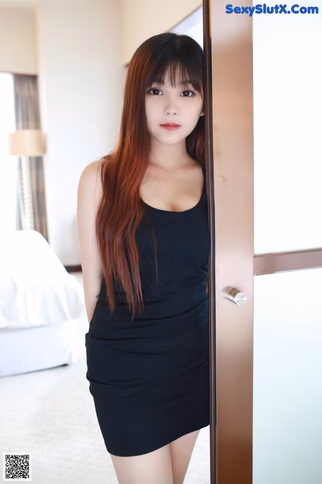 A woman in a black dress standing in front of a door.