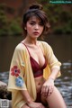 A woman in a red bikini sitting on a rock by the water.