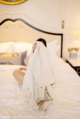 A woman sitting on a bed covered in a white sheet.