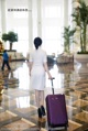 A woman in a white dress with a purple suitcase.