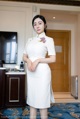 A woman in a white dress standing in a hotel room.