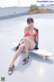 A woman in a red bikini sitting on a skateboard.