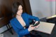 A woman in a blue suit sitting at a desk using a cell phone.