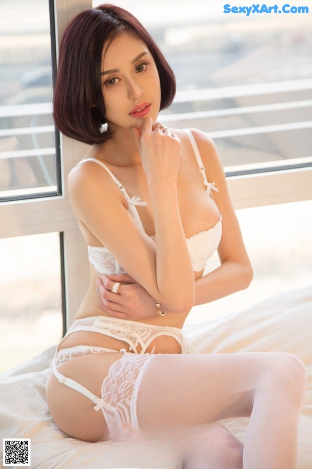 A woman in a white lingerie sitting on a bed.