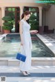 A woman in a white dress standing in front of a fountain.