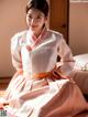 A woman in a pink and white hanbok sitting on a bed.