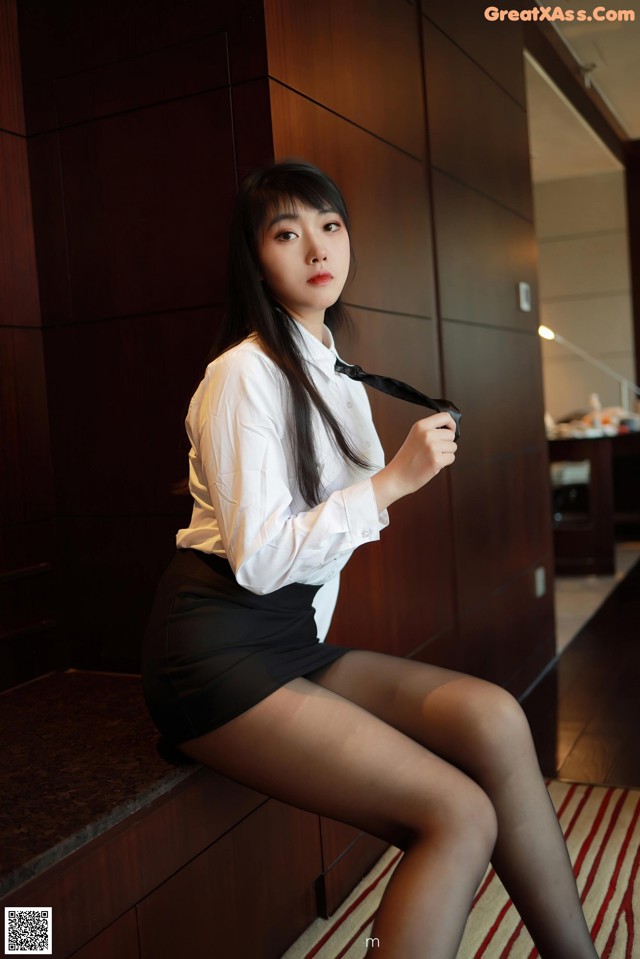 A woman in a white shirt and black skirt sitting on a counter.