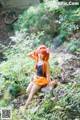 A woman in an orange dress sitting on a log in the woods.