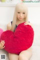 A woman sitting on a bed holding a red heart shaped pillow.