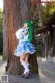 A woman with green hair standing next to a tree.