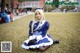 A woman in a blue and white dress sitting on the grass.