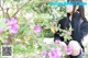 A young woman sitting in front of a bush of flowers.