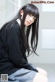 A woman with long black hair sitting on the floor.