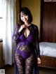 A woman in a purple lingerie posing in a hotel room.