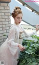 A woman in a white dress standing next to a plant.