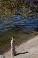 A woman in a long dress standing by the water.