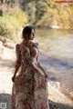 A woman in a floral dress standing by a river.