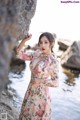 A woman in a floral dress leaning against a rock.