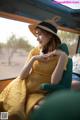 A woman in a yellow dress and hat sitting in the back of a car.