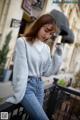 A woman in a gray sweater and jeans leaning against a railing.