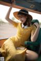 A woman in a yellow dress and hat sitting in a green chair.