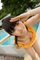 A woman in a yellow bathing suit standing next to a swimming pool.