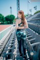 A woman in a sports bra top and leggings standing in a stadium.