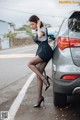 A woman leaning against a car on the side of the road.