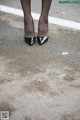 A woman wearing black high heels standing in a parking lot.