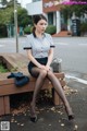 A woman sitting on a wooden bench in a parking lot.