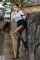 A woman leaning against a stone wall with her hand on her chin.