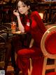 A woman in a red dress sitting at a table with a drink.