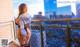 A woman standing on a balcony with a city in the background.