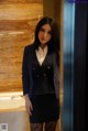 A woman in a business suit standing in a bathroom.