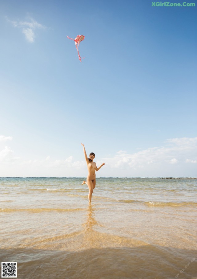 A naked woman flying a kite on the beach.
