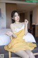 A woman in a yellow dress sitting on a bed.