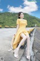 A woman in a yellow dress sitting on a concrete wall.