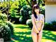 A naked asian woman standing in the grass in a garden.