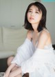 A woman sitting on a white couch wearing a white shirt.