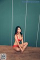 A woman in a red bikini sitting on a wooden floor.