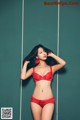 A woman in a red bra and panties leaning against a wall.