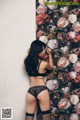 A woman in lingerie leaning against a wall with flowers.