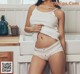 A woman in a white tank top and panties posing in a kitchen.