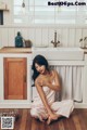 A woman sitting on the floor in a kitchen next to a sink.