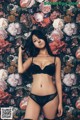 A woman in a black lingerie posing in front of a floral background.